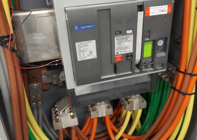 Electrical panel with colored cables connected to a main circuit breaker inside a metal enclosure.