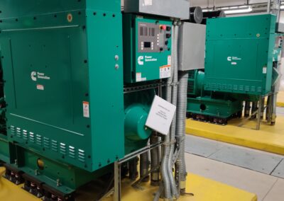 Two large green industrial generators with control panels are installed in a utility room with yellow flooring and exposed pipework.