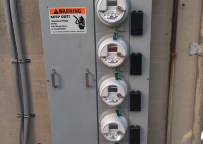 A panel of four electricity meters with a warning sign about hazardous voltage that reads, "KEEP OUT! Hazardous Voltage. Can Shock, Burn, or Cause Death. Keep out.