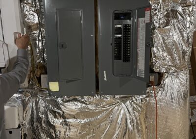 A person is opening one of two electrical circuit breaker panels mounted on a wall covered with reflective insulation material.